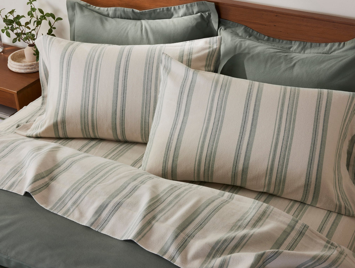 Close-up of Coyuchi Cloud Brushed Flannel pillowcases in ivory with sage green stripes on styled bed.
