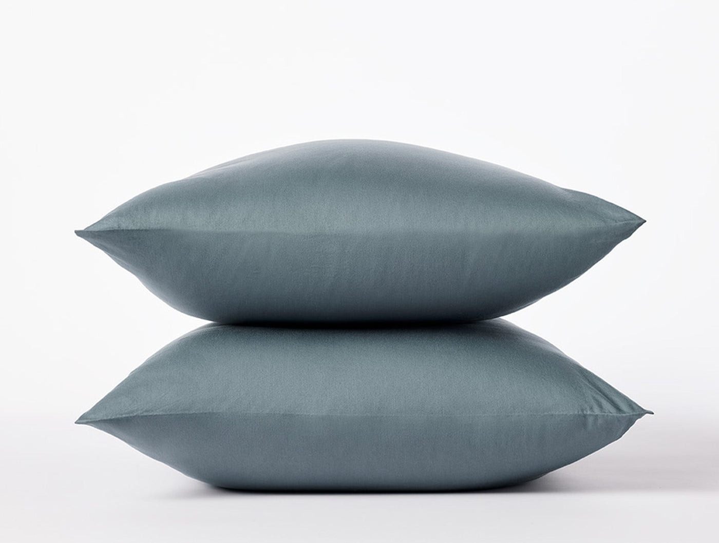 Two slate blue Coyuchi Cloud Soft Sateen pillowcases stacked against a white background.