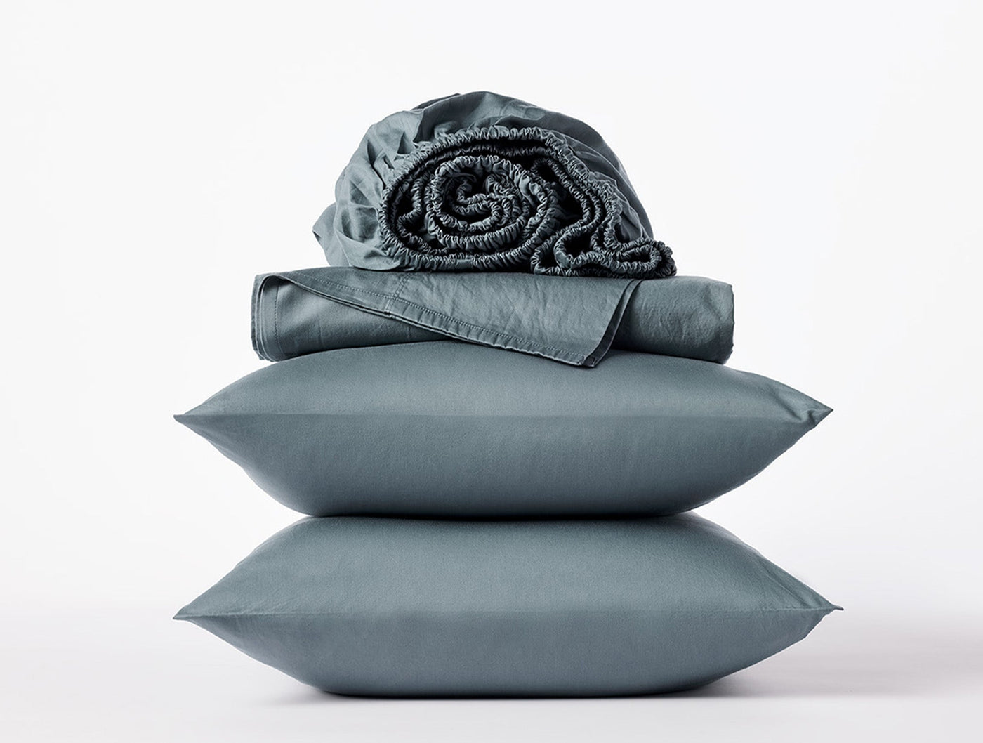 Close-up of stacked slate Coyuchi Cloud Soft Sateen pillowcases with folded and rolled sheets.