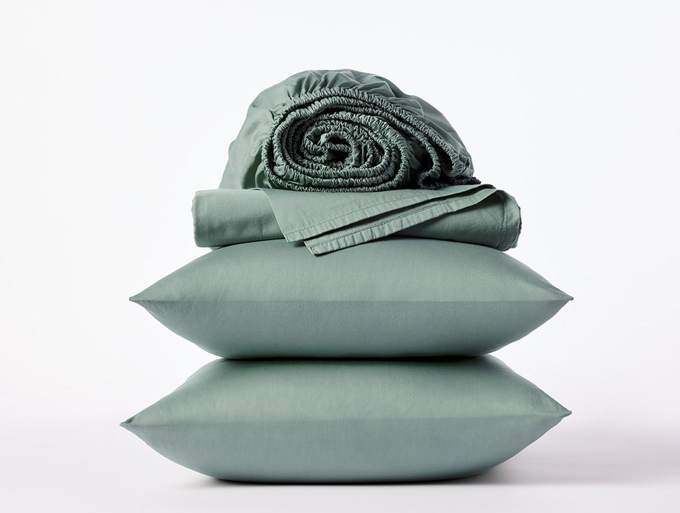 Sage green sateen sheet set styled with stacked pillowcases and rolled fitted sheet.
