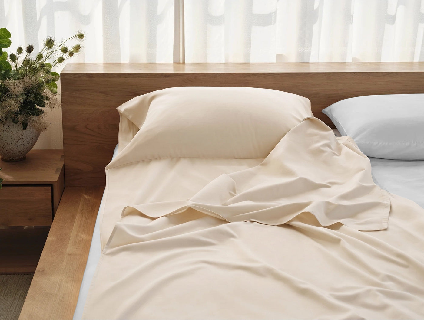 Coyuchi Cloud Soft Sateen travel sack in ivory, draped loosely over a bed in a sunlit room.