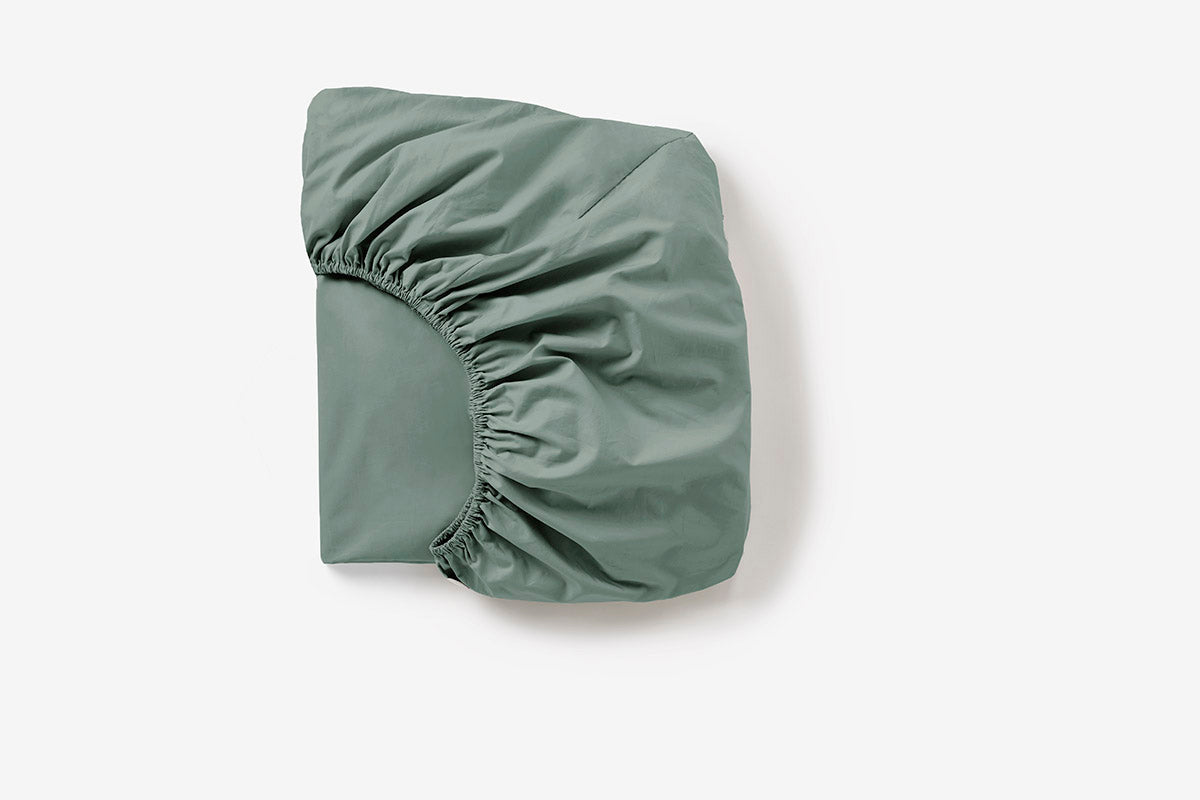 Sage green fitted sheet folded to show elasticated corners and sateen sheen.