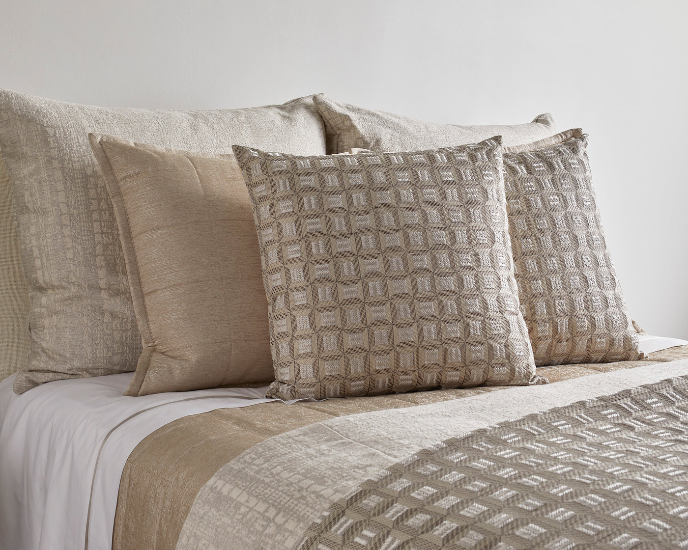 Ann Gish Collonade pillows in champagne, geometric woven pattern, styled on a neutral bed.
