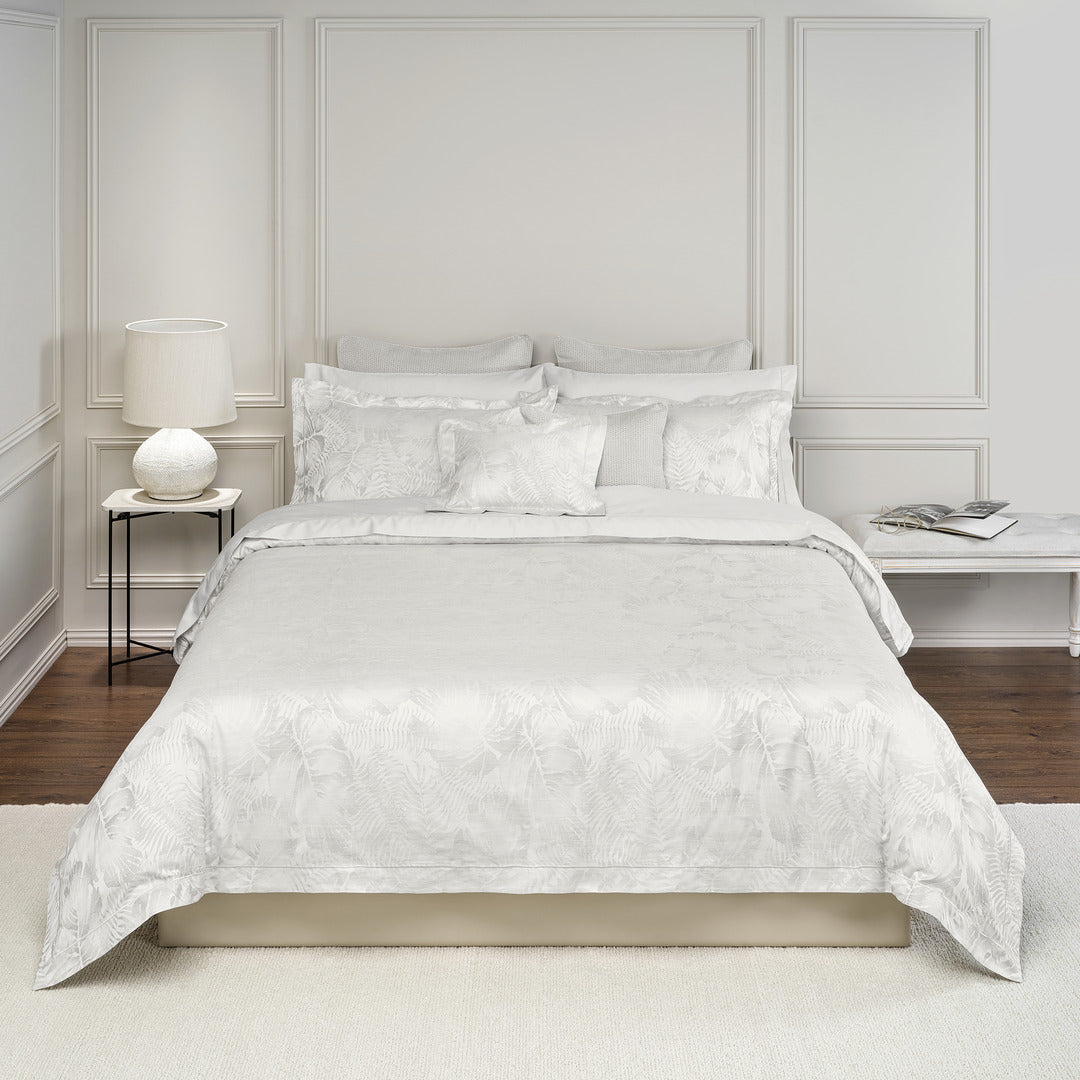 White jacquard duvet cover with tropical leaf pattern on a styled bed in a neutral bedroom.