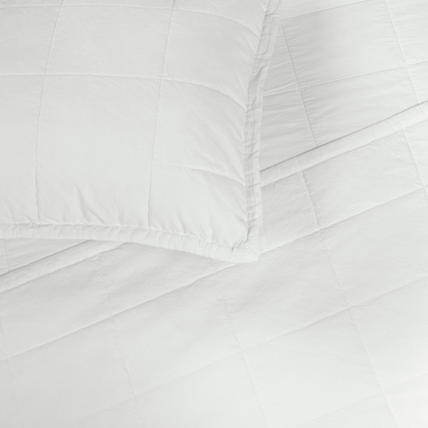 Close-up corner of Ann Gish Cotton Canvas Coverlet Set in white with grid stitching detail.