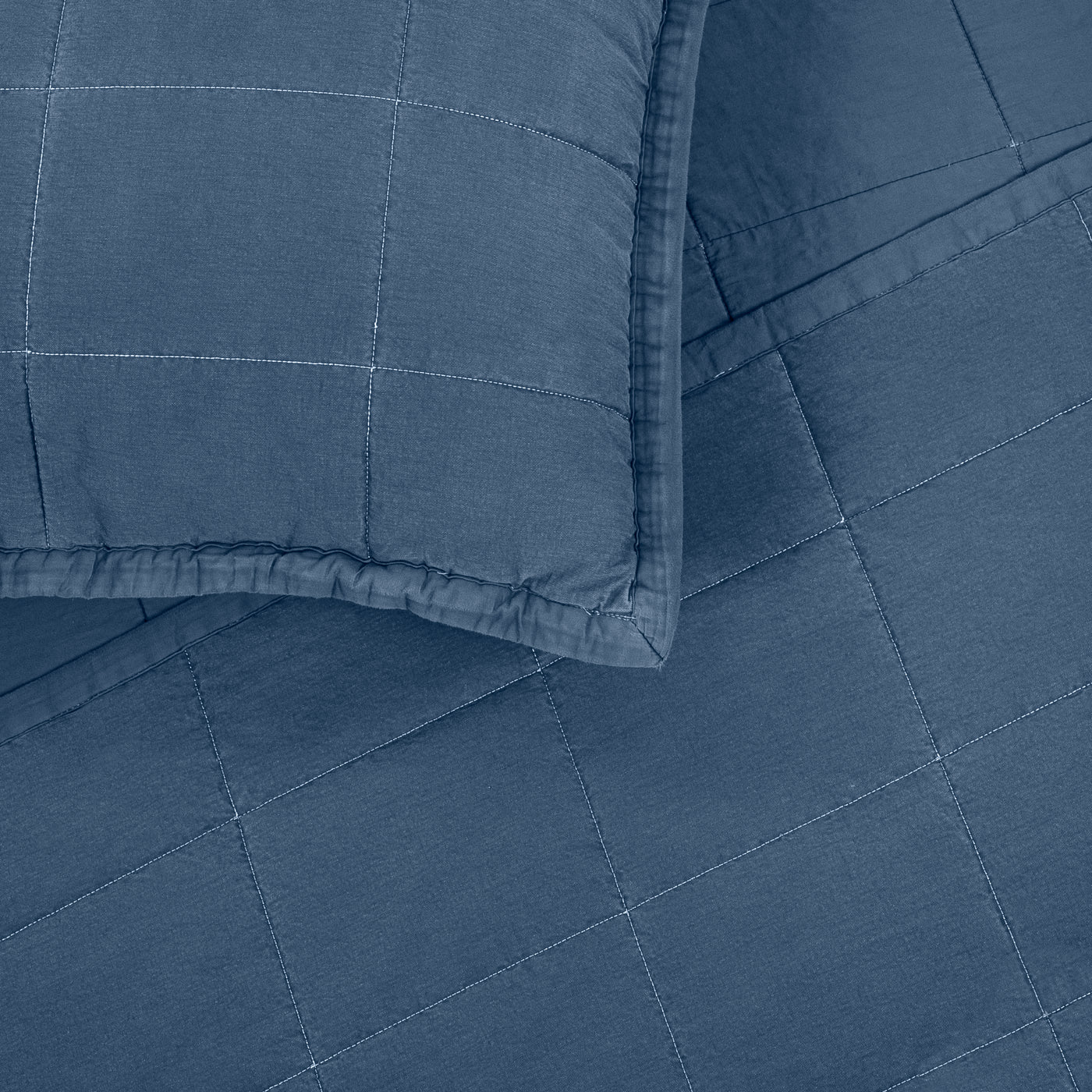 Close-up of steel blue quilted cotton coverlet corner with matching pillow sham detail.