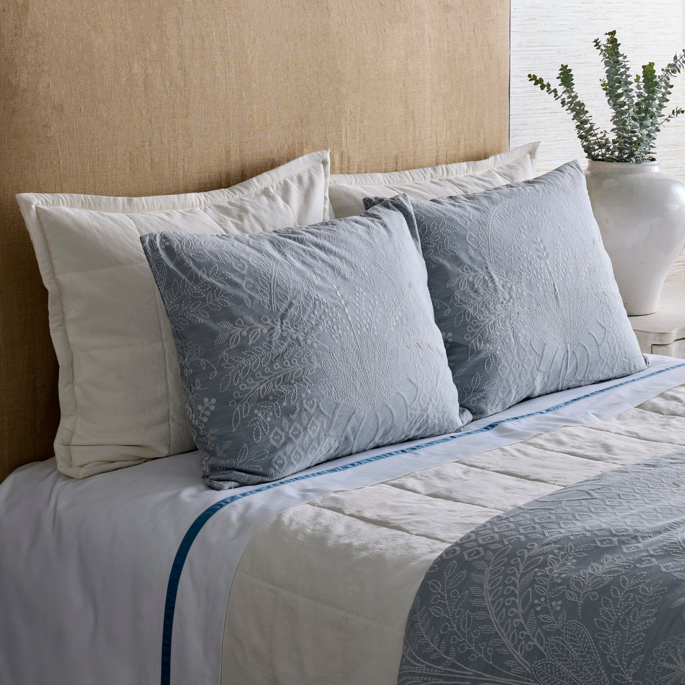 Pale blue quilted coverlet set styled on bed, featuring two embroidered euro shams in foreground.