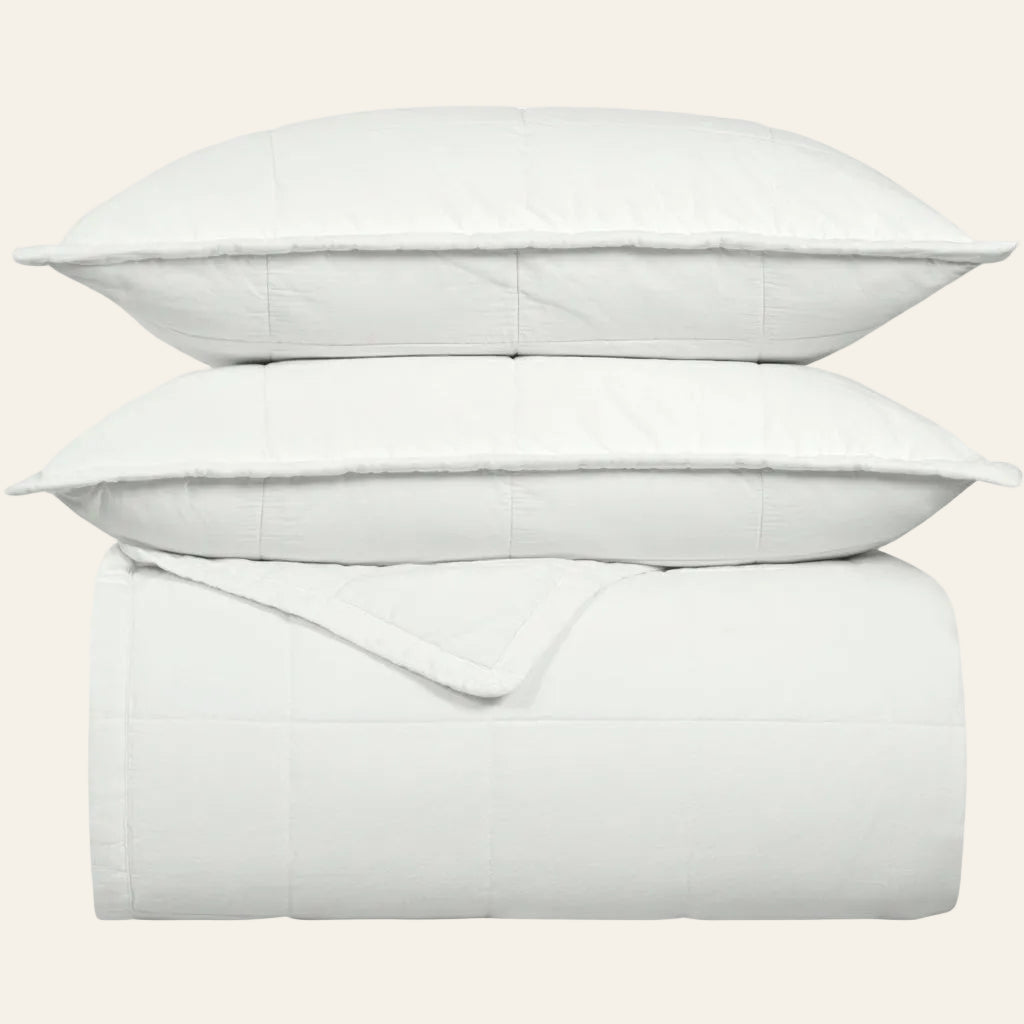 Ann Gish Cotton Canvas coverlet set in white, neatly folded and stacked with two matching shams.