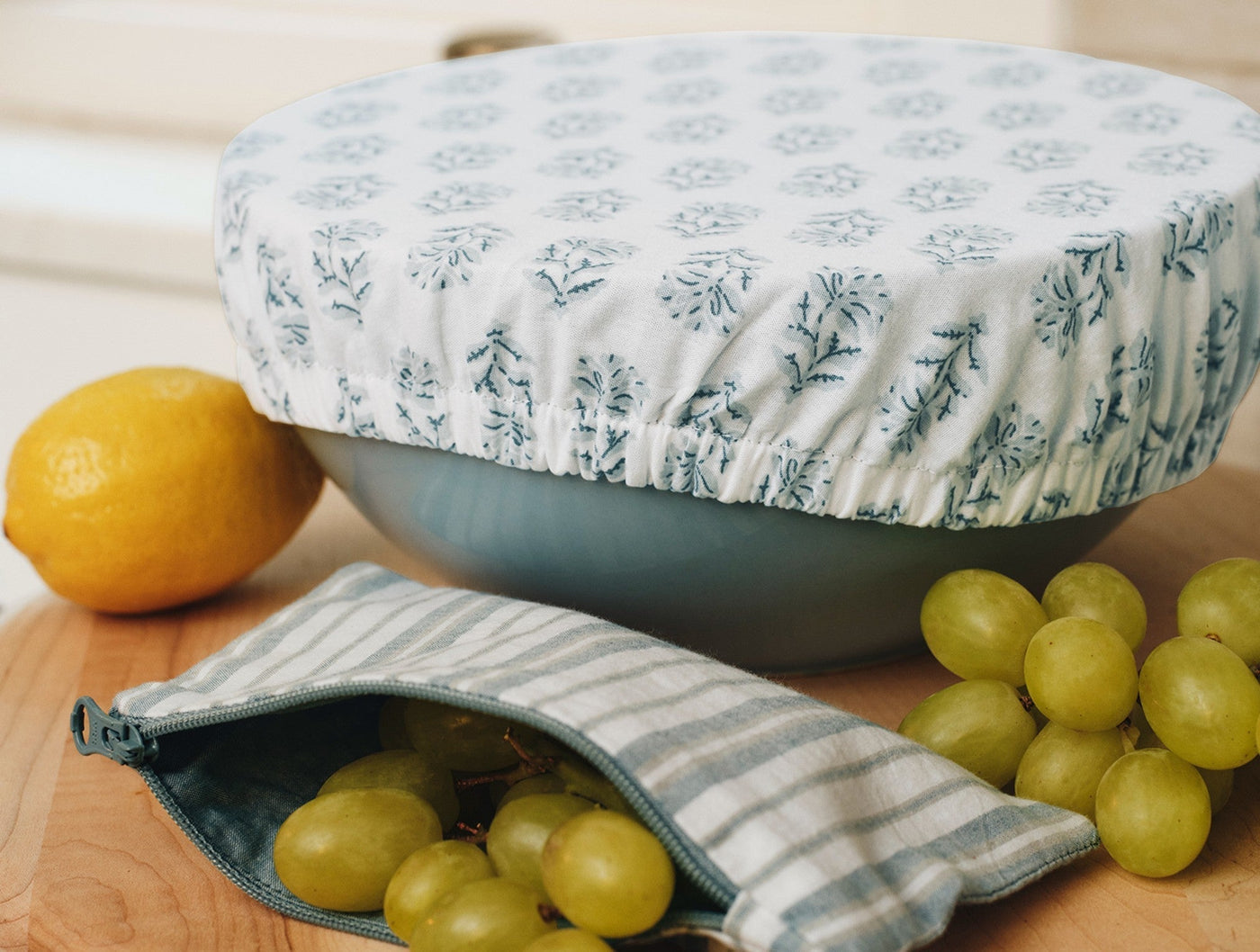 Close-up of Coyuchi bowl cover with blue floral block print over a bowl, styled with grapes and lemon.