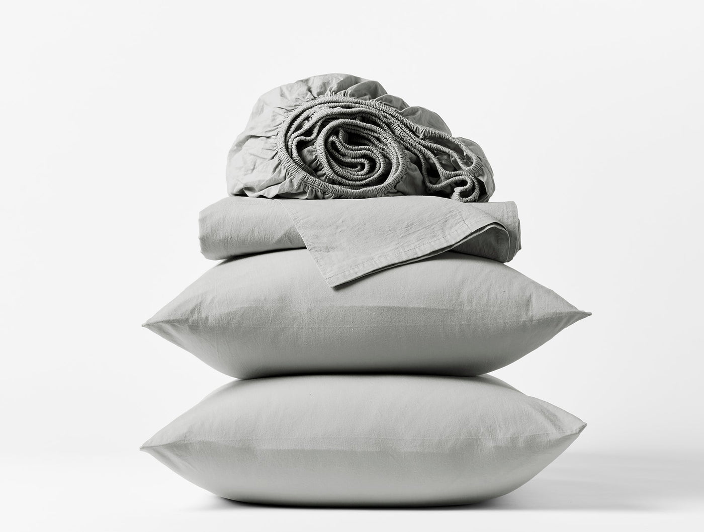 Stacked silver Coyuchi Crinkled Percale pillowcases and folded sheet set against white background.