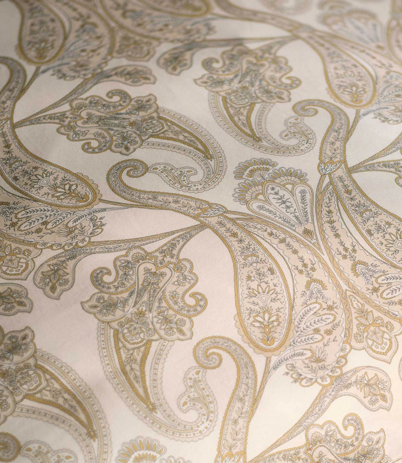 Close-up of gold and silver paisley print on ivory cotton fabric.