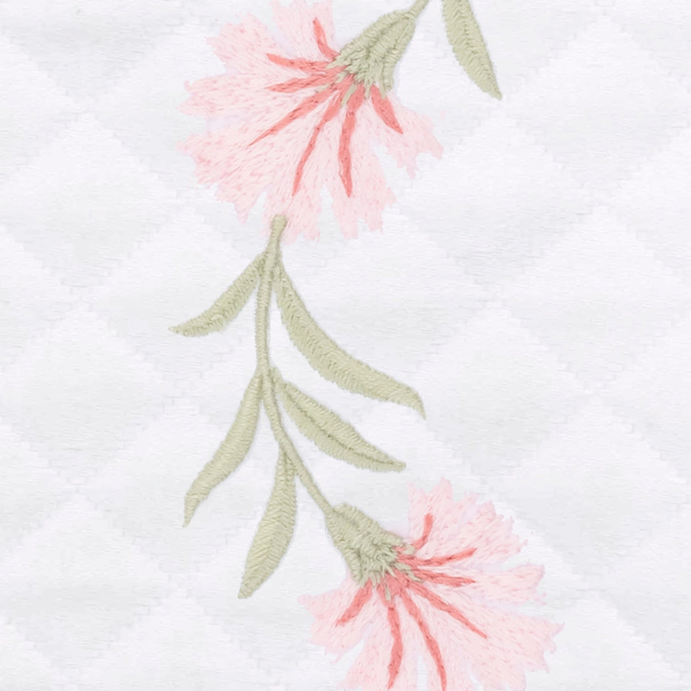 Close-up of blush floral embroidery with sage green stems on white diamond matelassé weave.