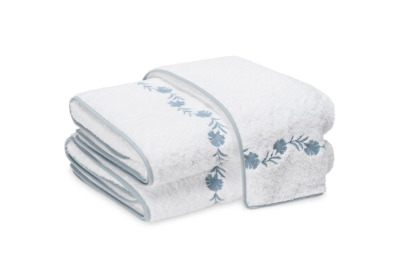 Matouk Daphne white bath sheets with blue floral embroidery, neatly folded and stacked.