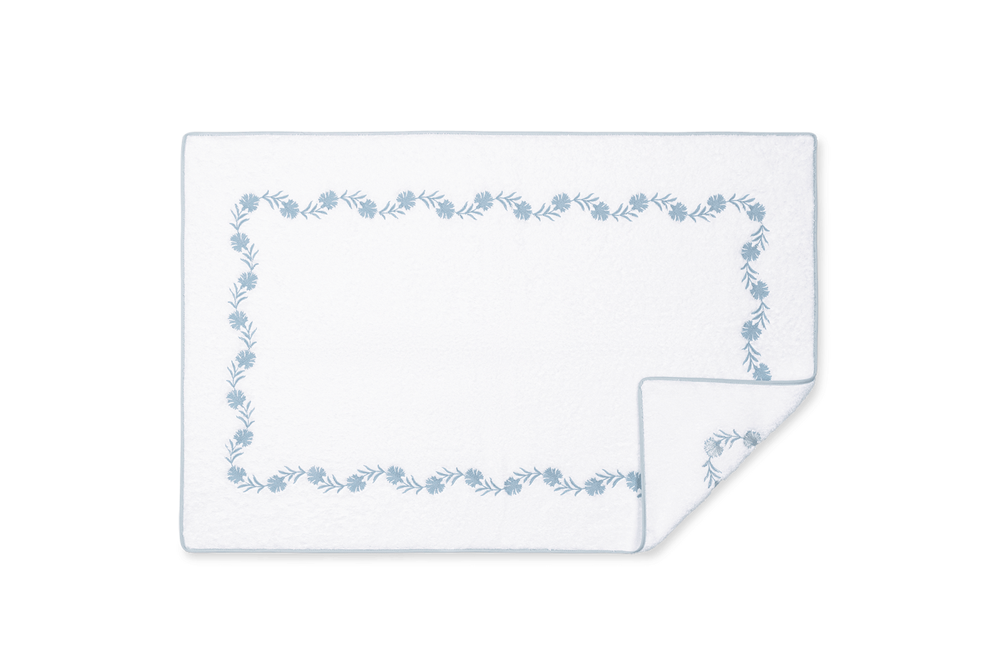 Corner detail of Matouk Daphne tub mat showing blue floral embroidered border on white.