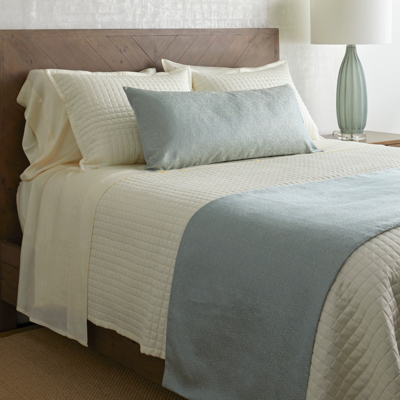 Ann Gish Dapple bed finisher in ivory and spa blue styled on a made bed with quilted texture.