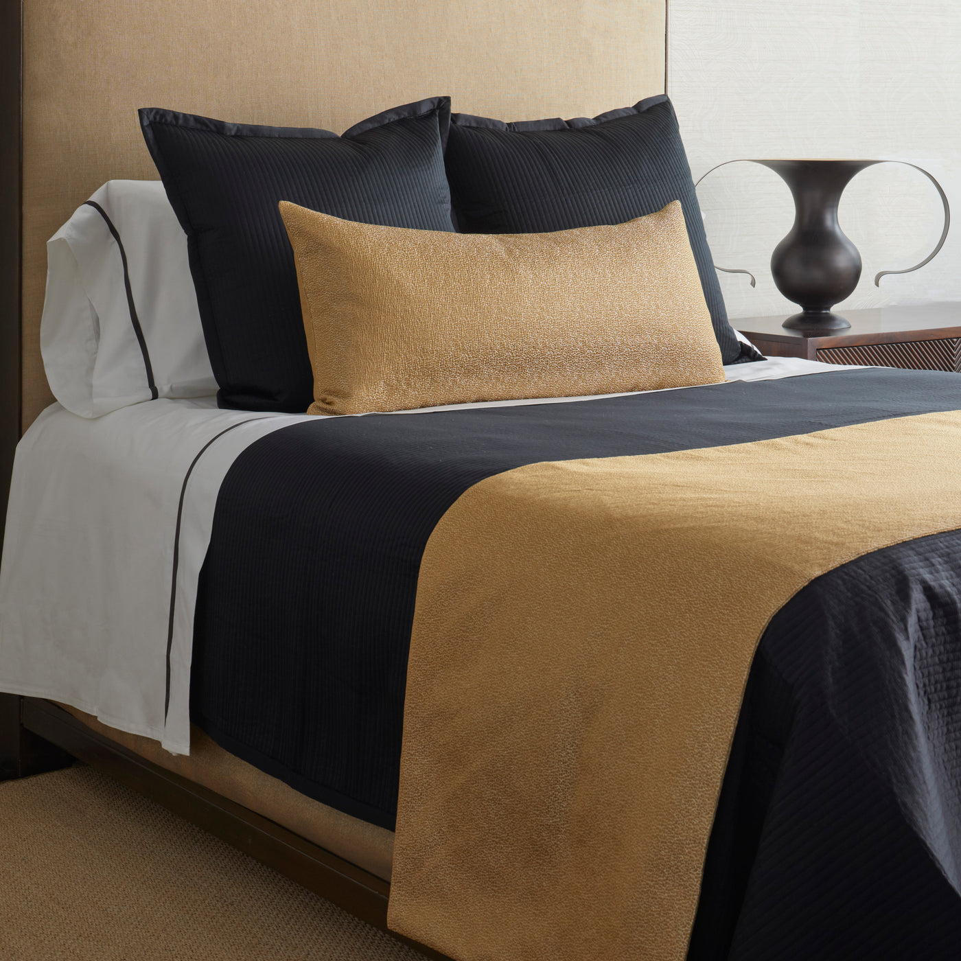 Ann Gish Dapple bed finisher set in gold and navy, styled on a made bed with pillows.