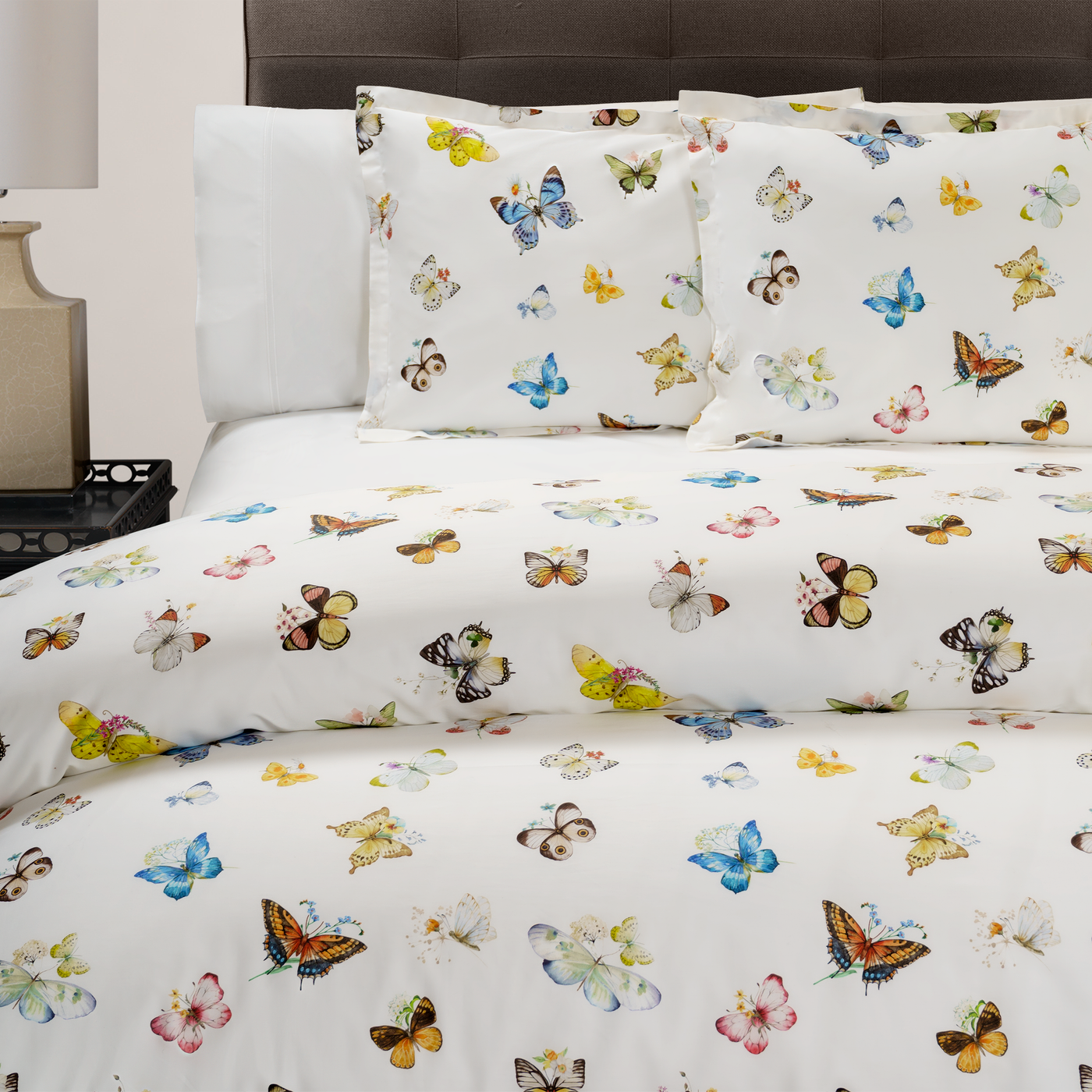 DEA Volante duvet set in ivory cotton with multicolor butterfly print, styled on bed.
