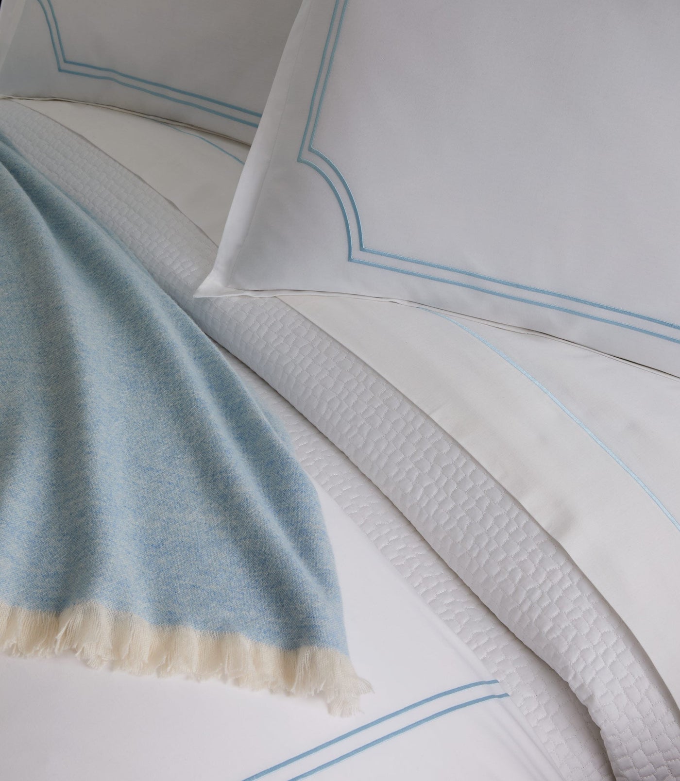 Close-up of sky blue embroidered border detail with fringed cashmere throw draped alongside.