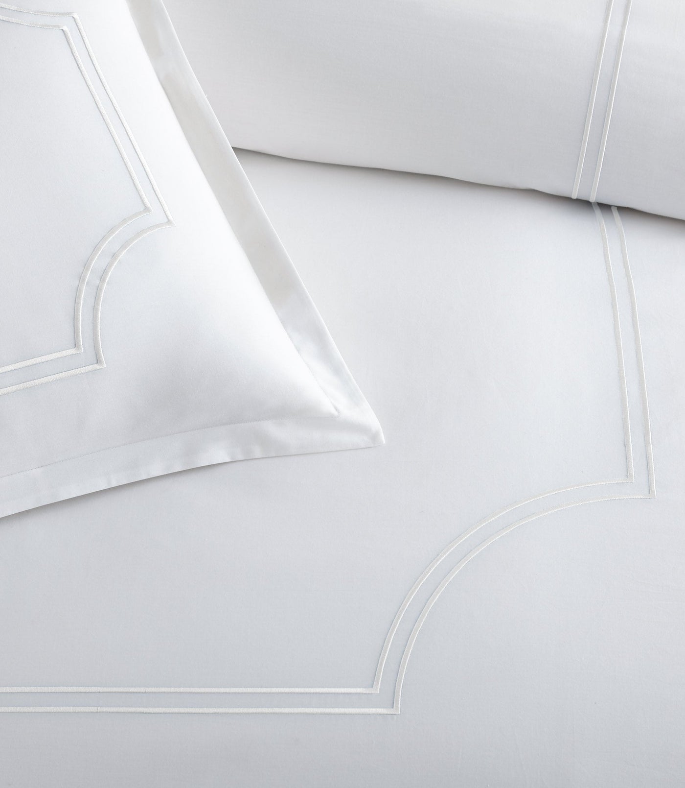 Close-up of white-on-white embroidered arch border detail on crisp cotton duvet cover.