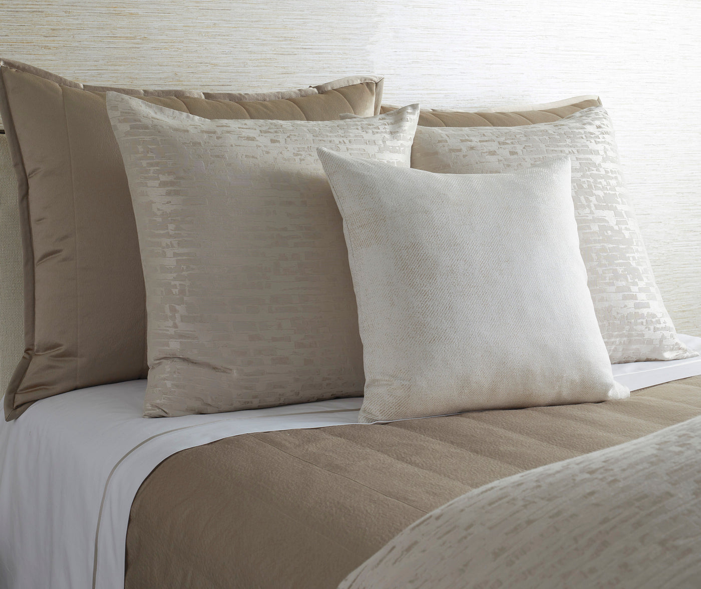 Ivory and taupe bedding ensemble with textured geometric pillow styling on made bed.