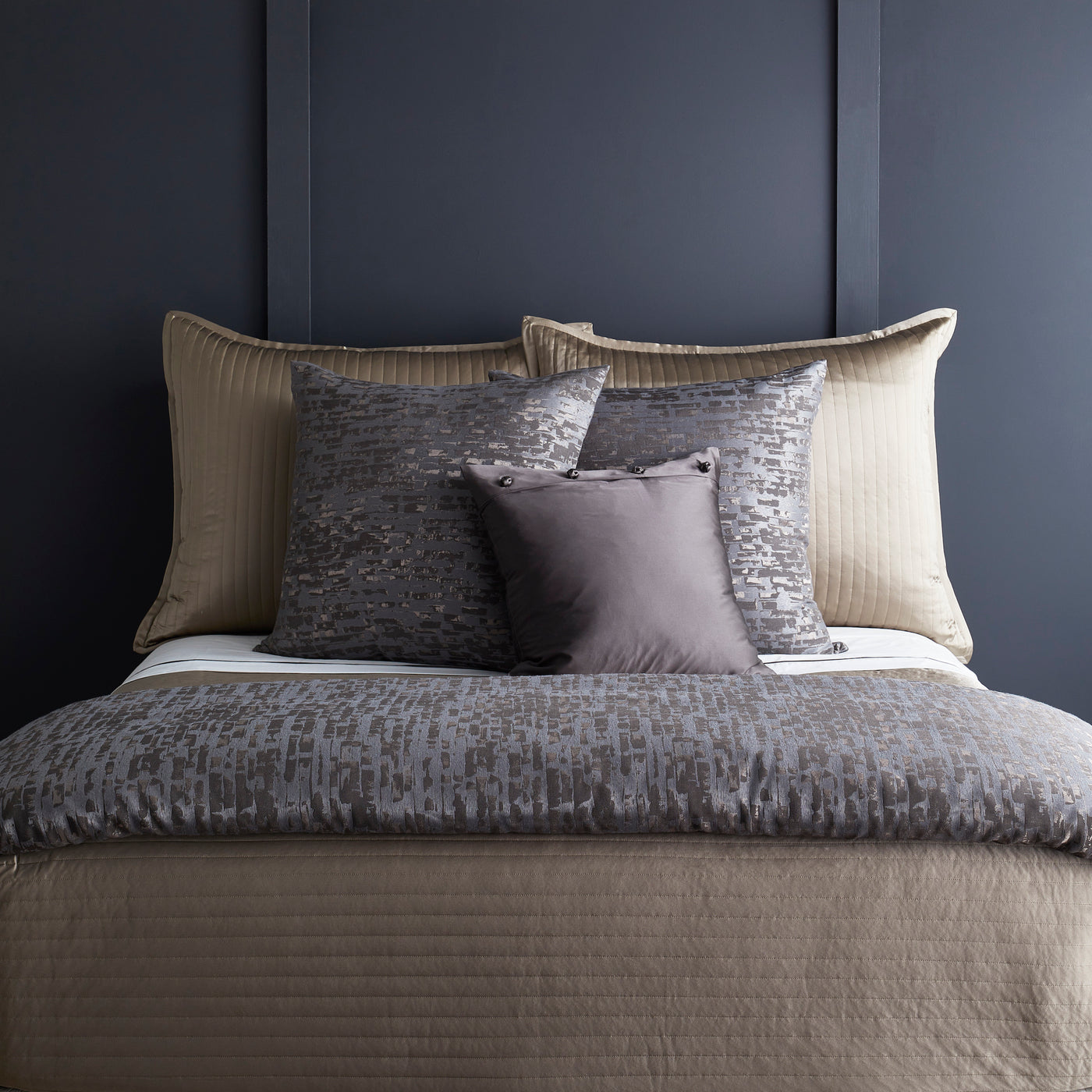 Delphi duvet styled on bed with layered charcoal and champagne pillows against navy wall.