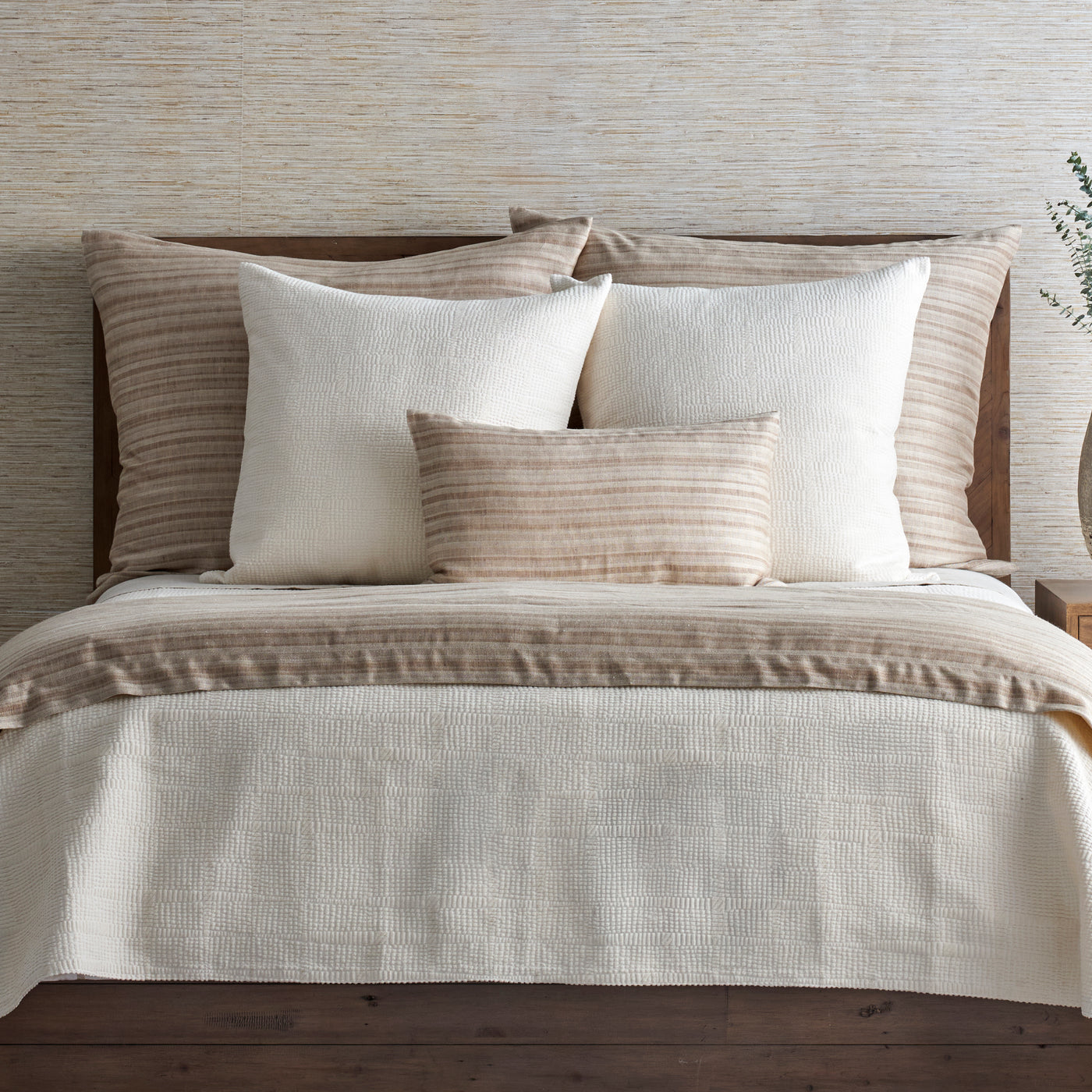 Ivory duvet and tan striped shams styled on a wood bed with layered pillows.