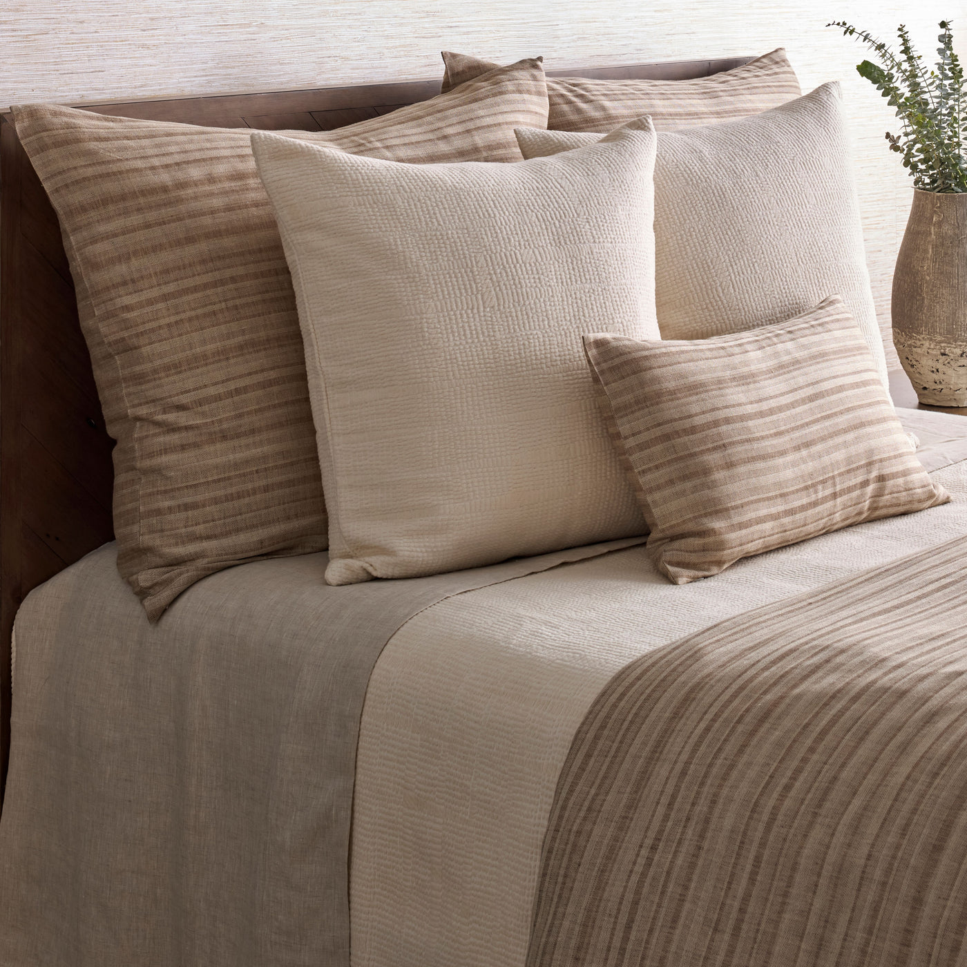 Ann Gish Doria duvet styled on bed with layered taupe and sand tone pillows in a bedroom setting.