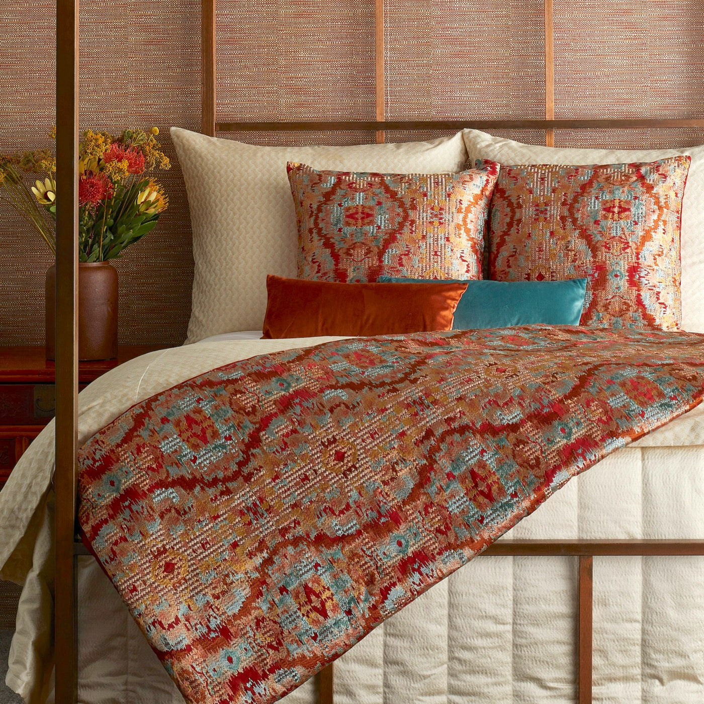Ann Gish Dowry pillow in terracotta and teal ikat pattern, styled on a made bed.