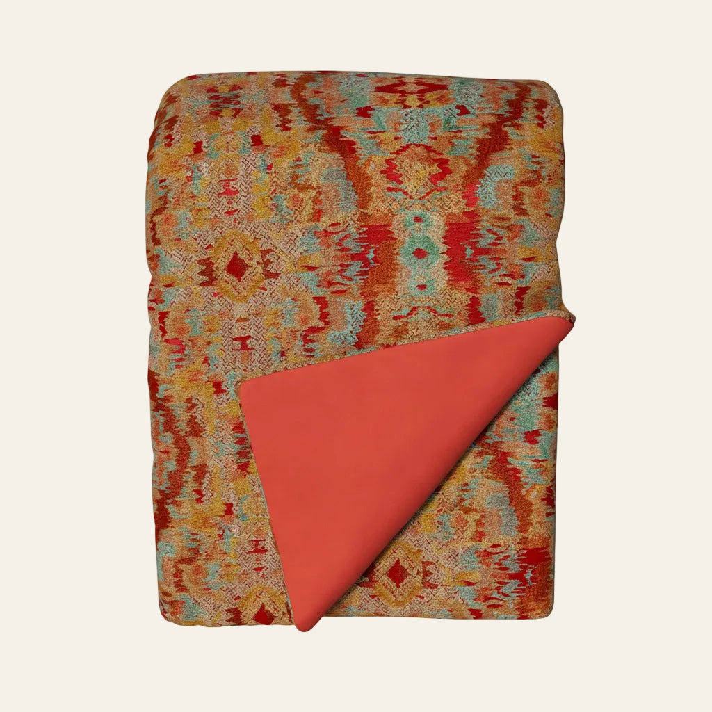Ann Gish Dowry throw, coral ikat-patterned front with solid coral reverse, folded flat.
