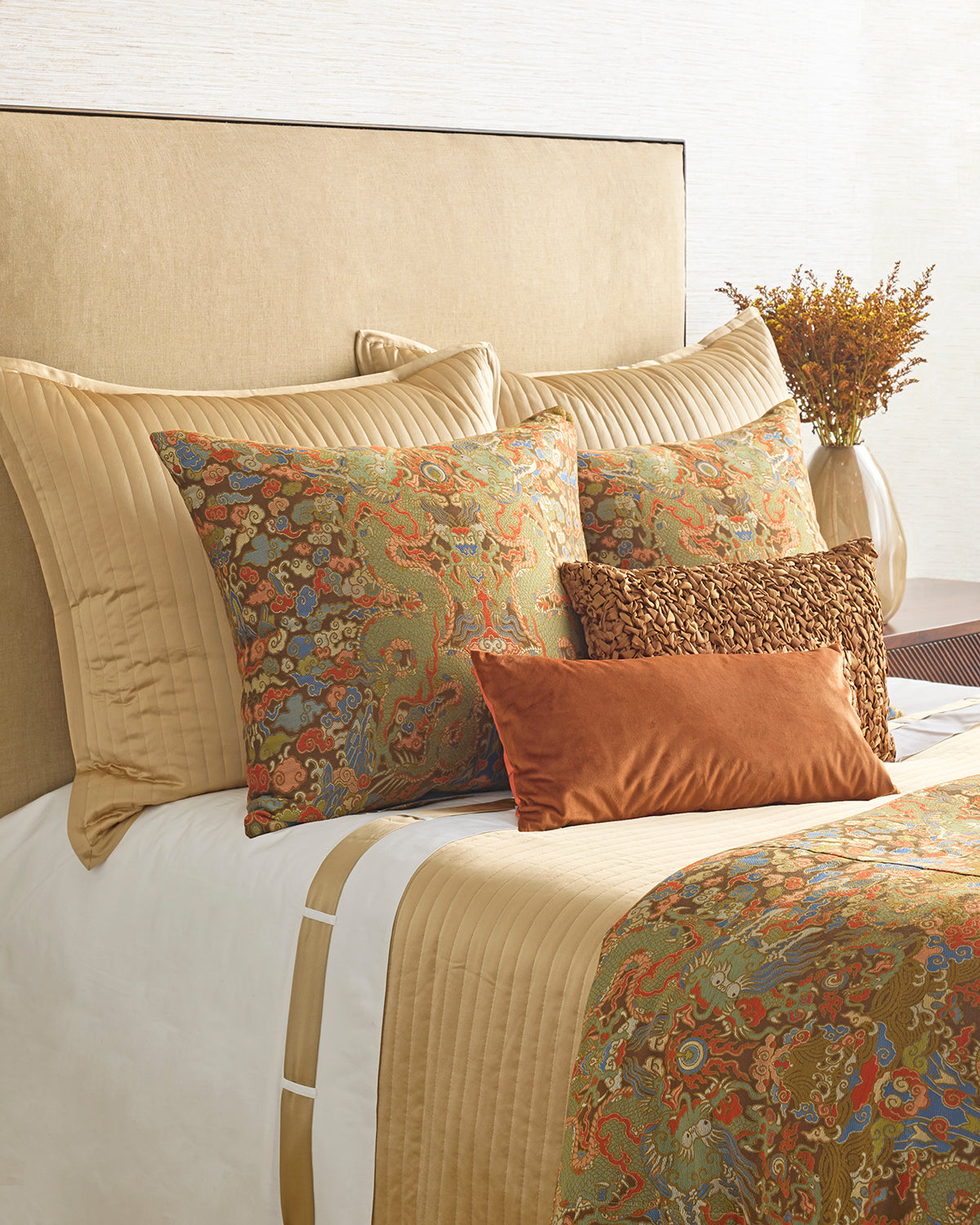 Bed styled with floral and dragon-motif bedding in gold, rust, and sage with layered accent pillows.