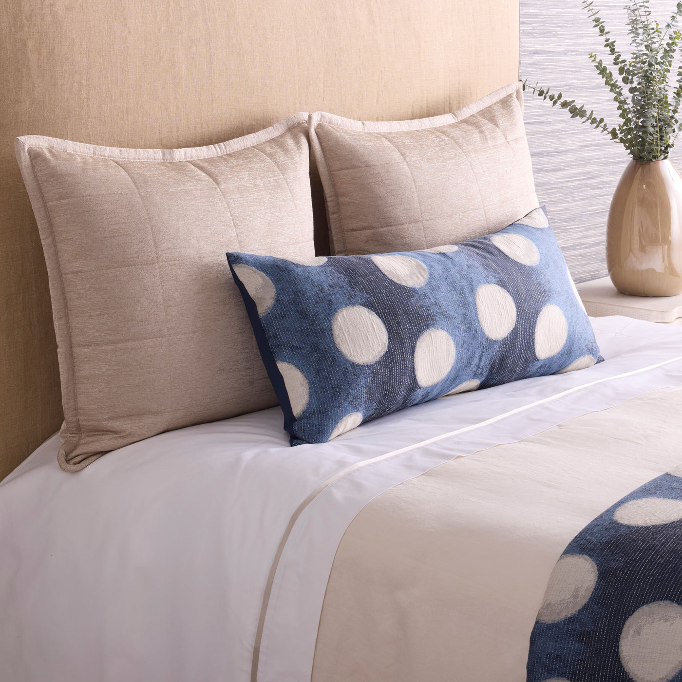 Ann Gish Eclipse lumbar pillow in denim blue with ivory polka dots on a styled bed.