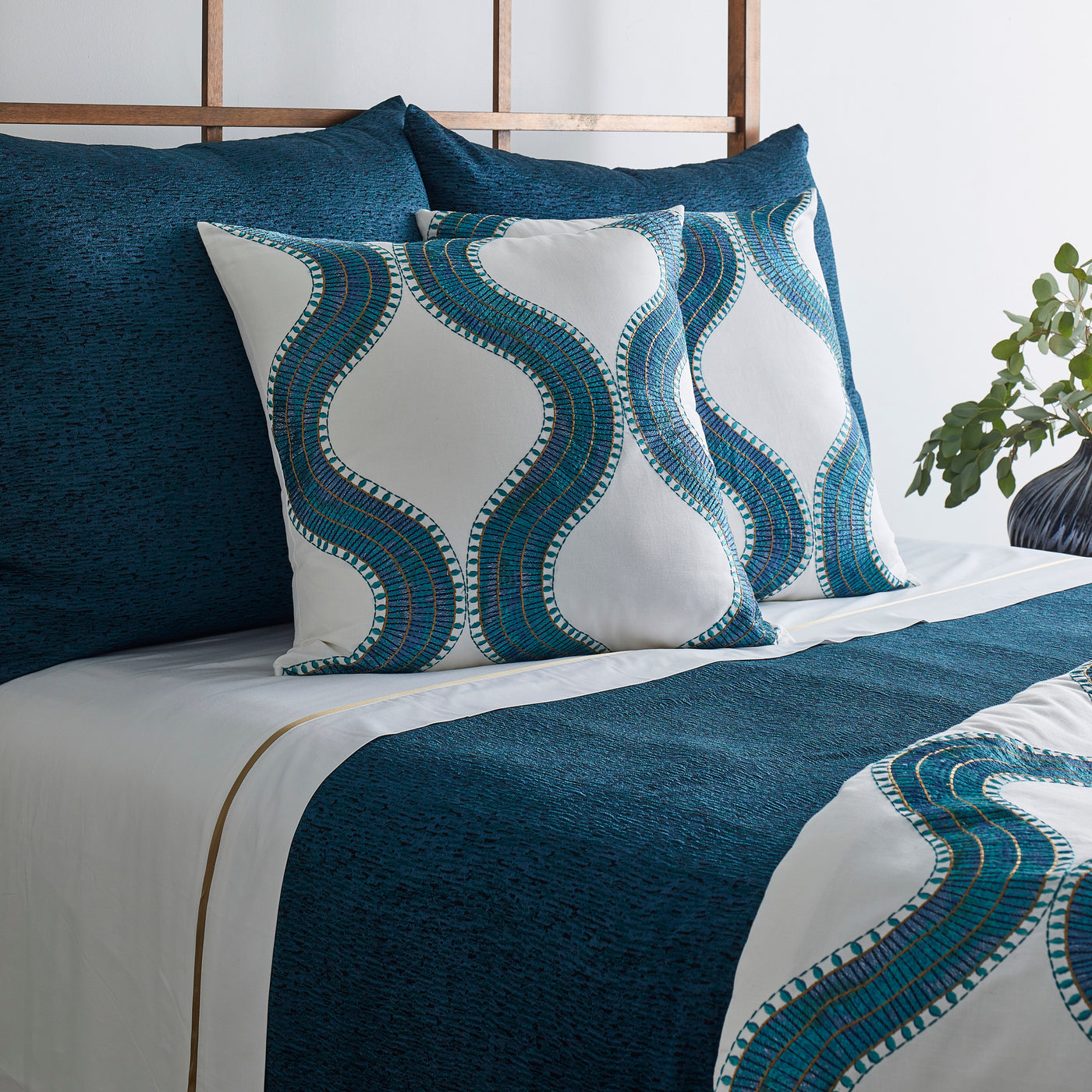 Ann Gish Egyptian Collar pillows in teal and white ogee pattern styled on a made bed.