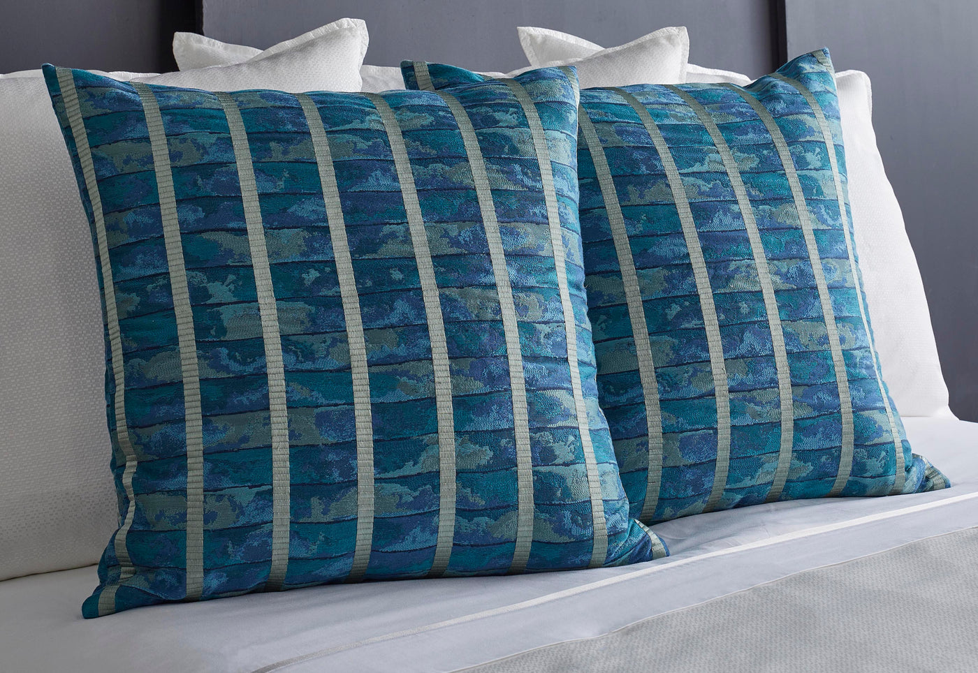 Ann Gish Egyptian Faience pillows in teal blue with vertical stripe pattern on white bed.