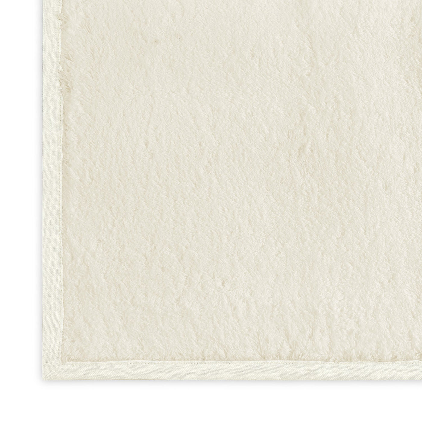 Close-up corner detail of ivory terry wash cloth with smooth woven border edge.