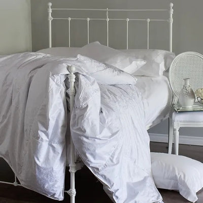 St. Geneve Europa white duvet draped over an iron bed frame with pillows