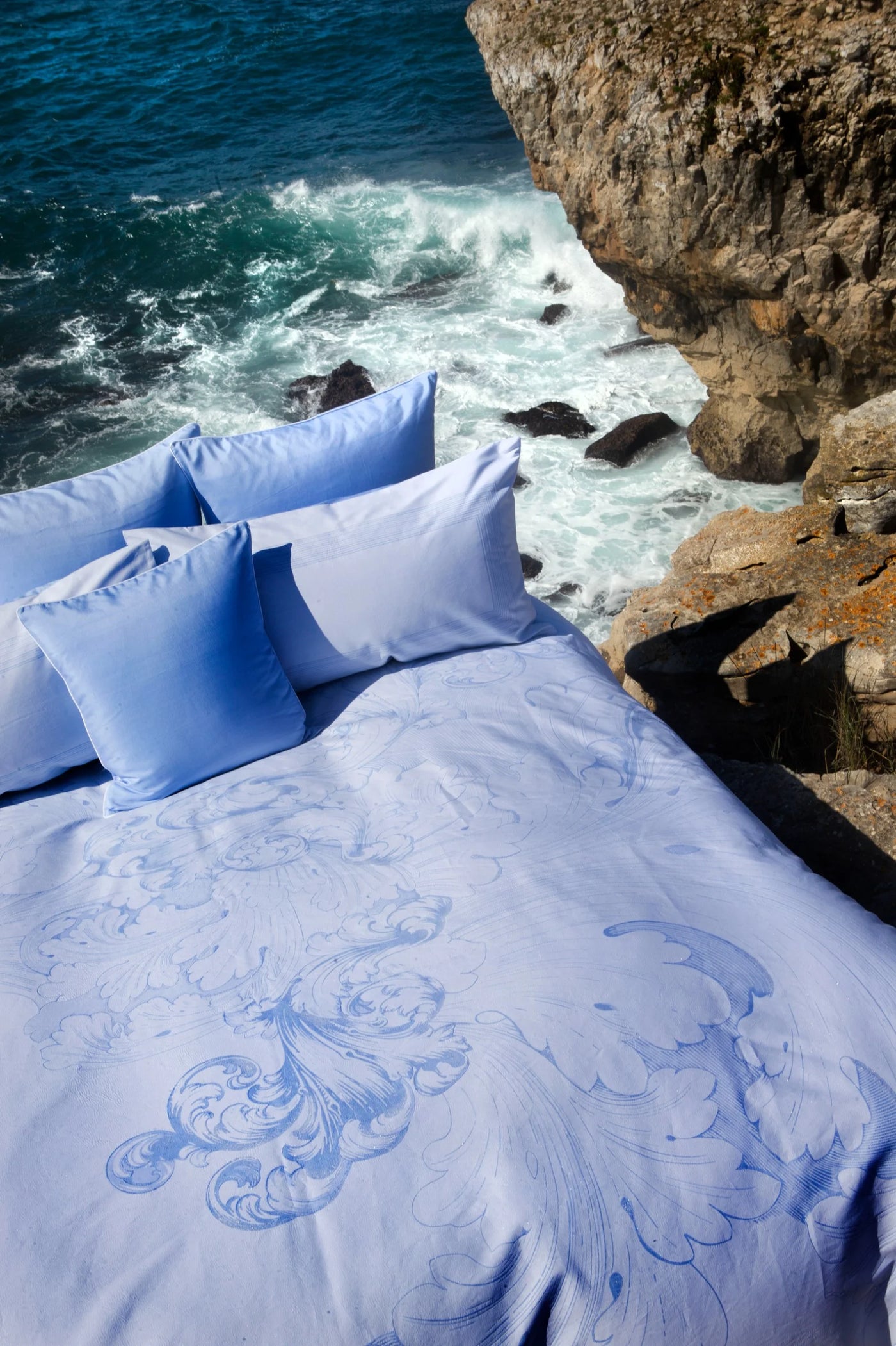 Periwinkle duvet cover with tonal baroque embroidery, styled on rocky coastal cliffside.