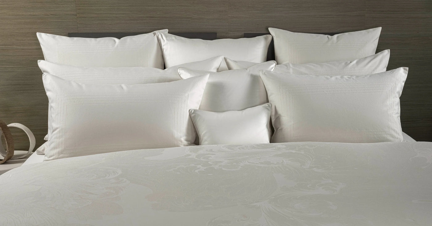 Close-up of ivory jacquard pillowcases and shams layered on a made bed.