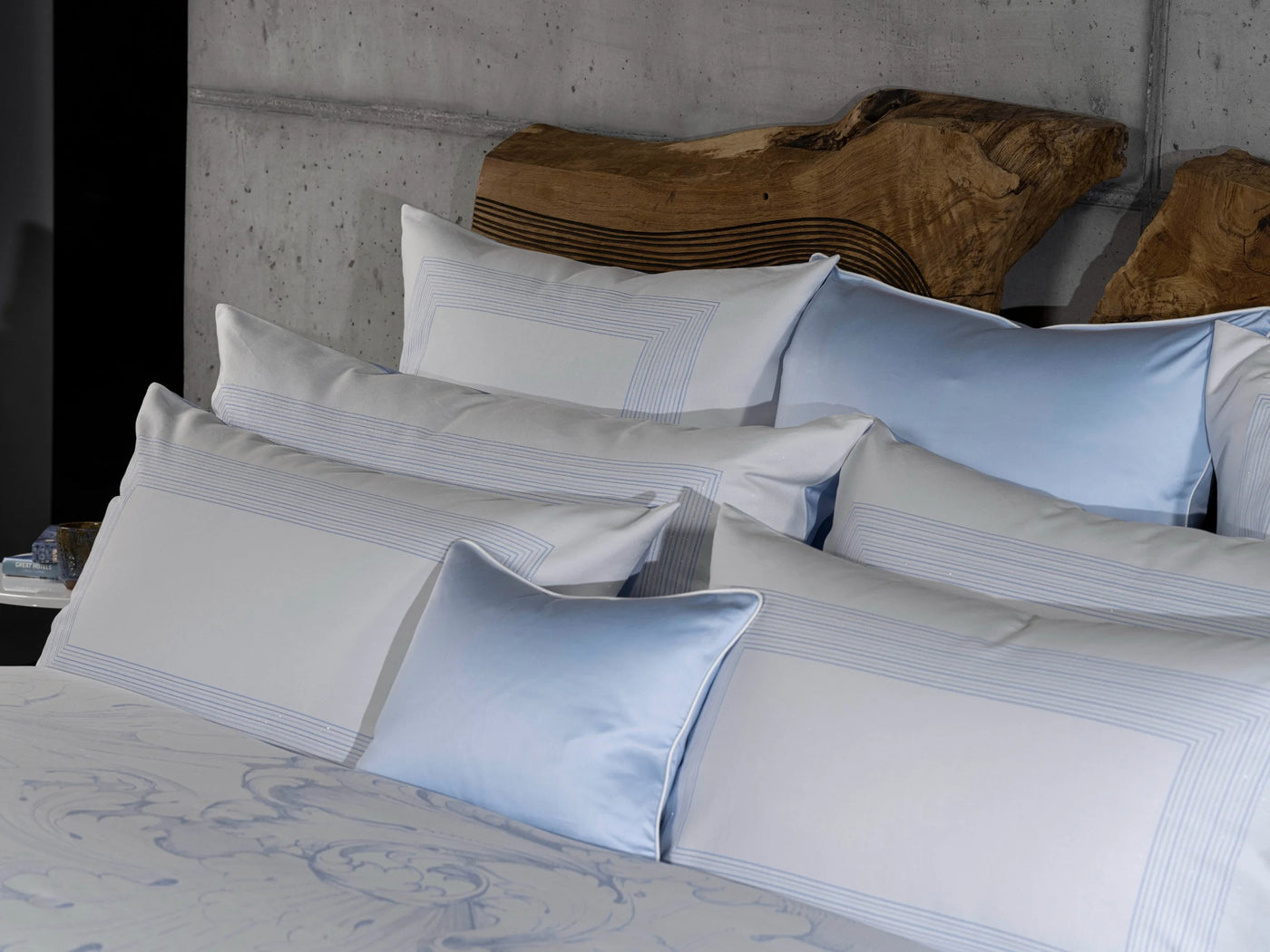 Pale blue and white pillowcases with satin border detail, styled on a layered bed.