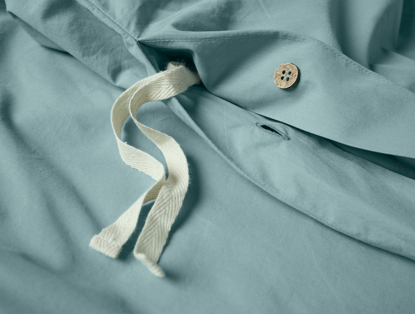 Close-up of Coyuchi Refined Percale duvet cover in ocean blue with tie closure and button detail.