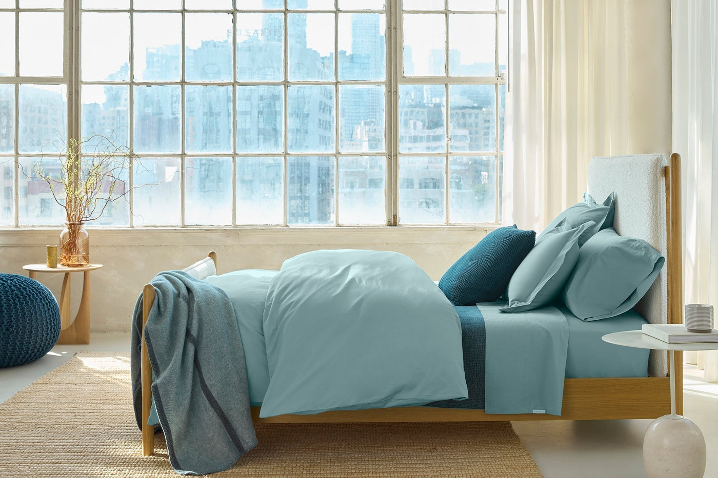 Coyuchi Refined Percale sham styled on bed with teal bedding, natural wood frame, loft windows.