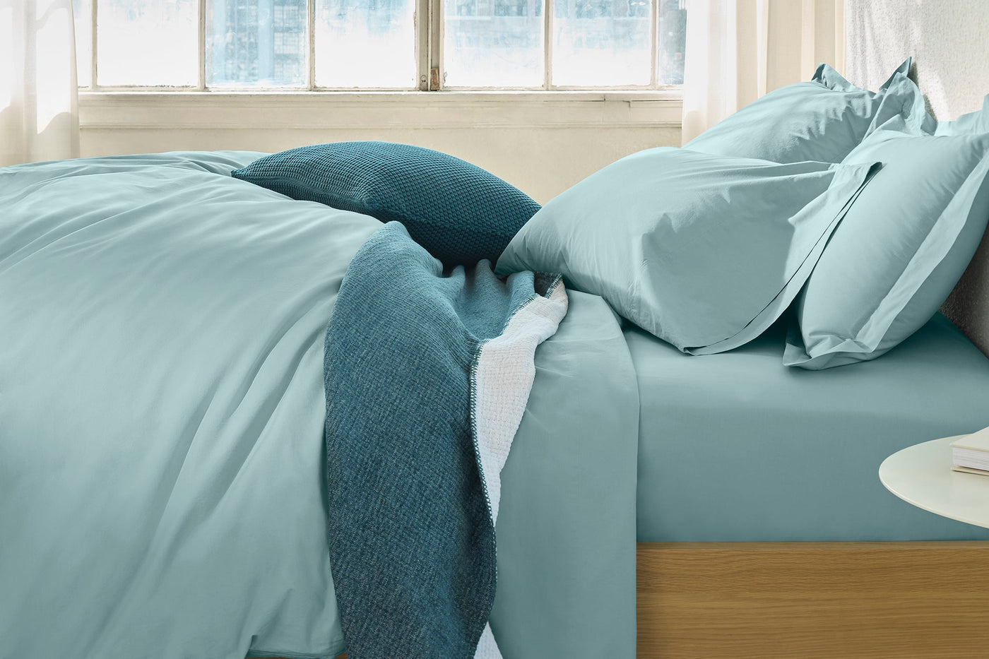 Pale aqua percale fitted sheet on a styled bed with teal accent pillows, natural light.