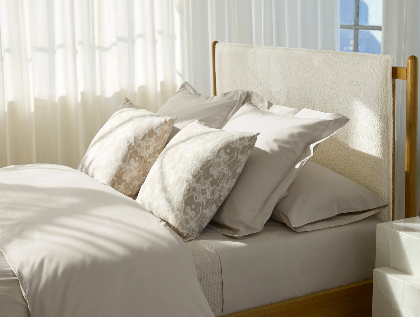 Coyuchi Refined Percale sheet set styled on a bed with layered ivory and taupe pillows.