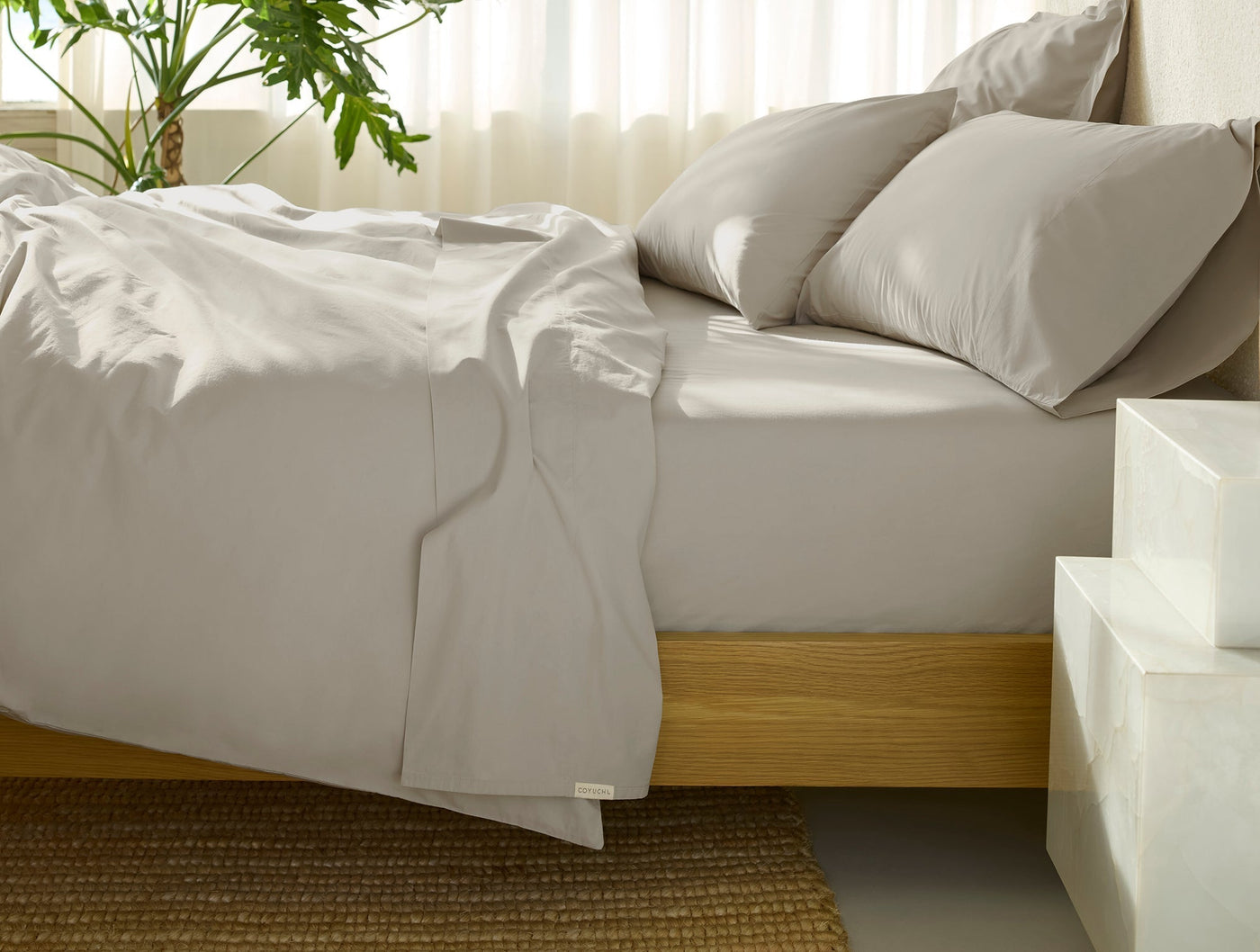 Dove grey percale sheet set draped casually over a wood-frame bed with matching pillowcases.