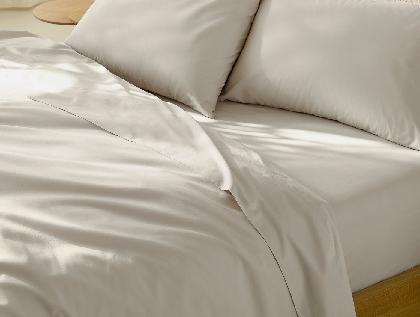 Ivory percale sheet set styled on bed, showing lustrous smooth surface and natural light drape.