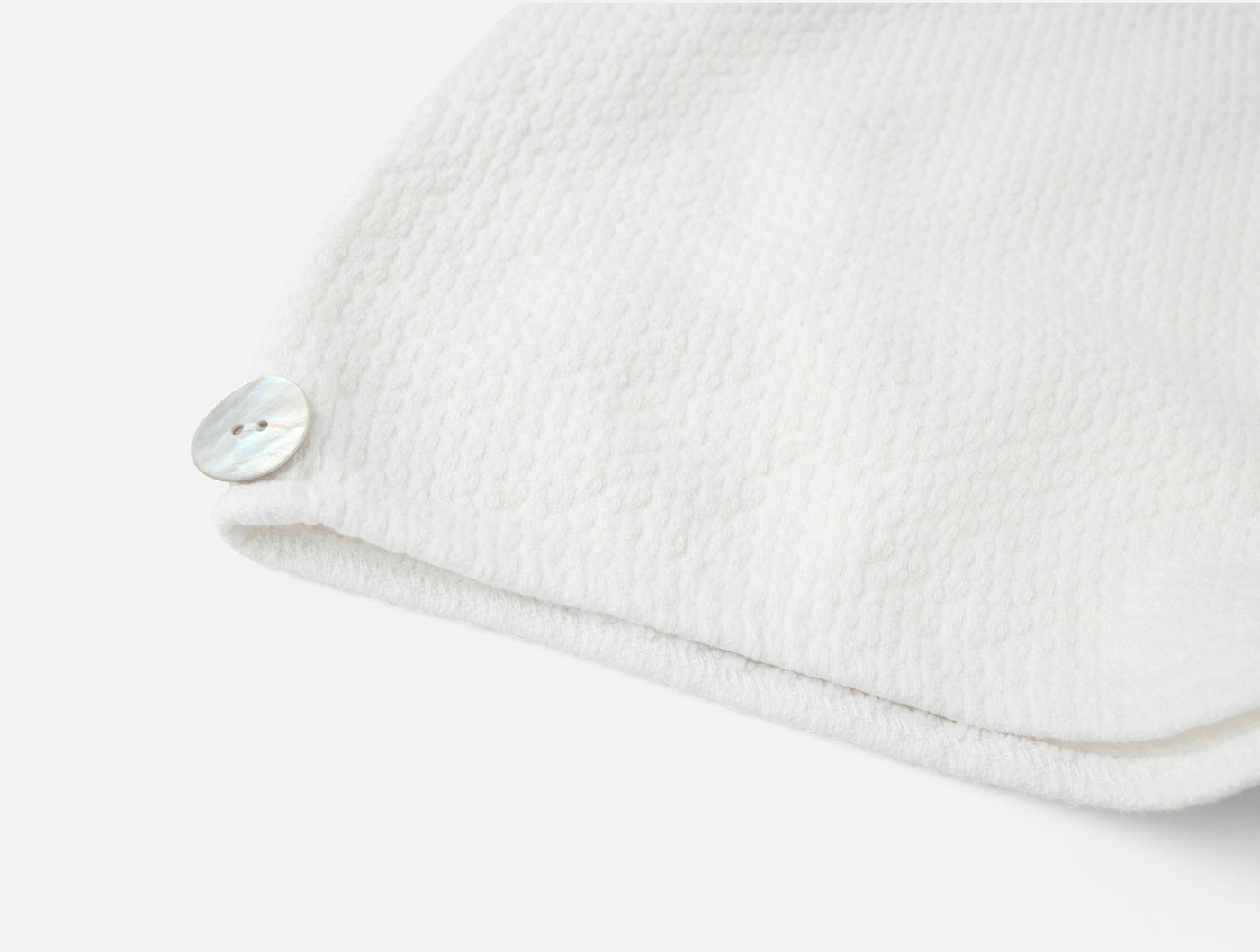 Close-up of white textured hair wrap corner with shell button closure.