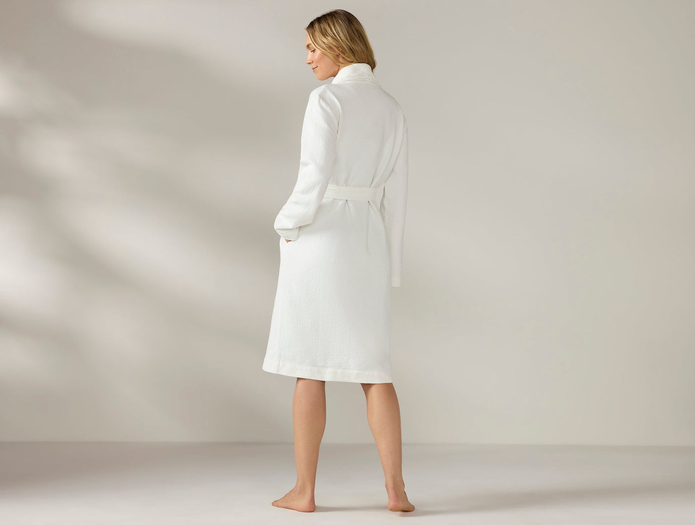 Woman wearing Coyuchi Adriatic robe in white, rear view showing belted waist and knee length.