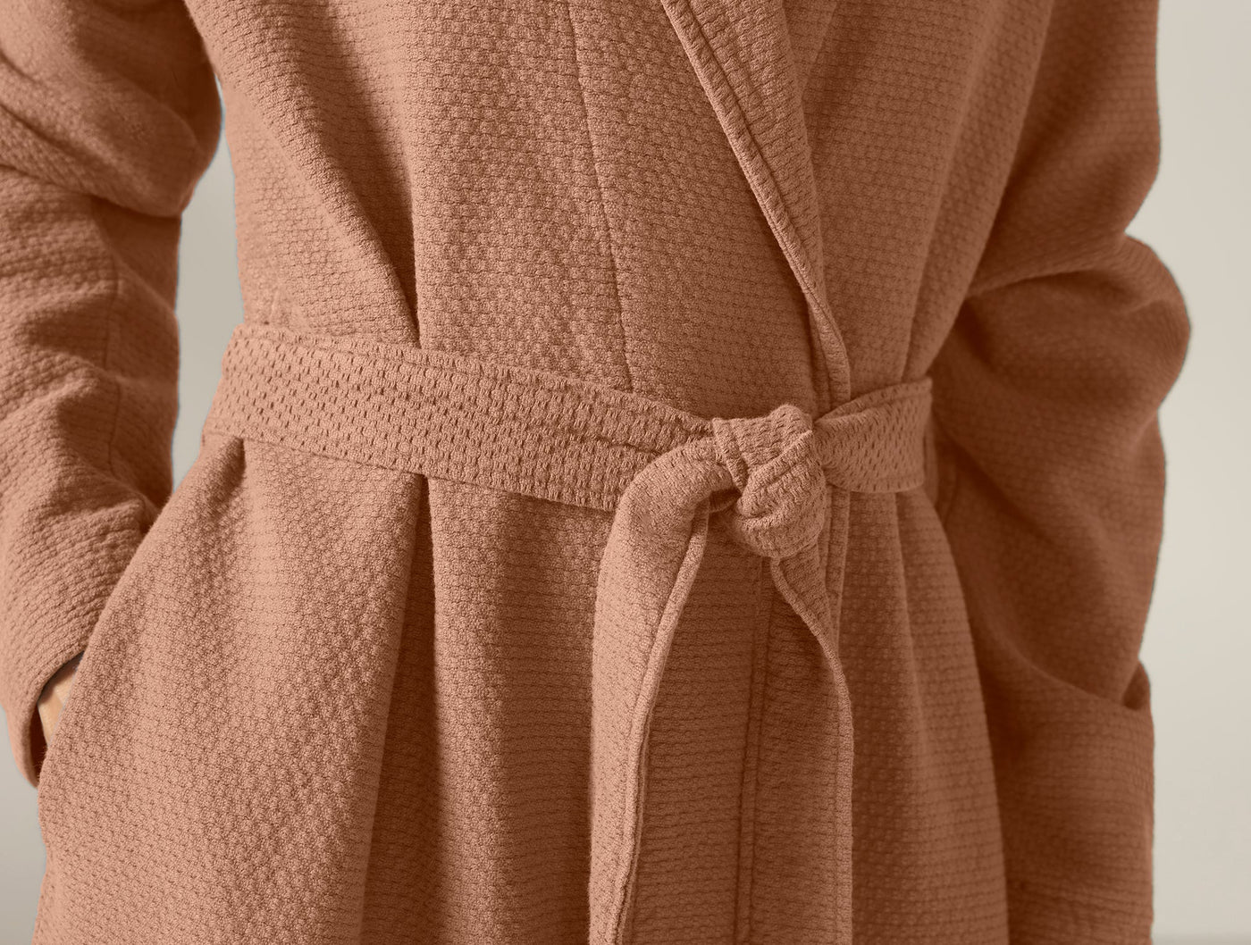 Close-up of tied waffle-knit belt at waist of Coyuchi robe in terracotta.