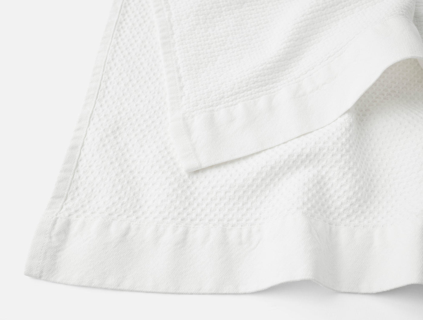 Close-up of Coyuchi Adriatic bath towel corner showing white waffle texture and satin border hem.