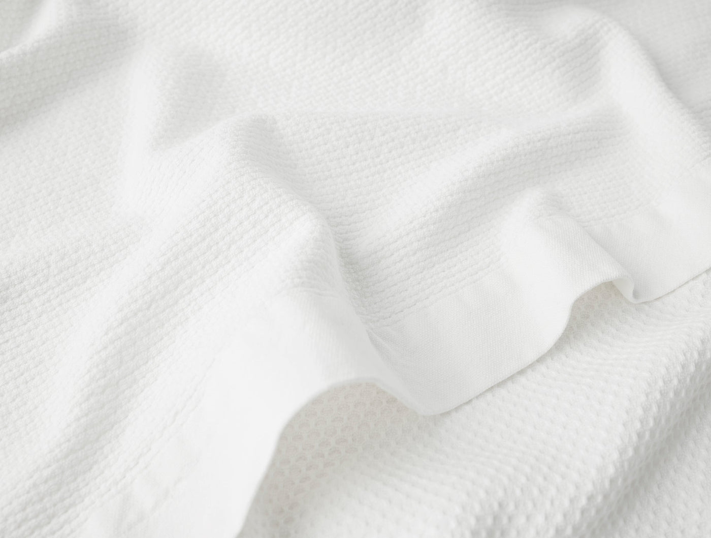 Close-up of white waffle-weave cotton texture with soft draping and subtle sheen.