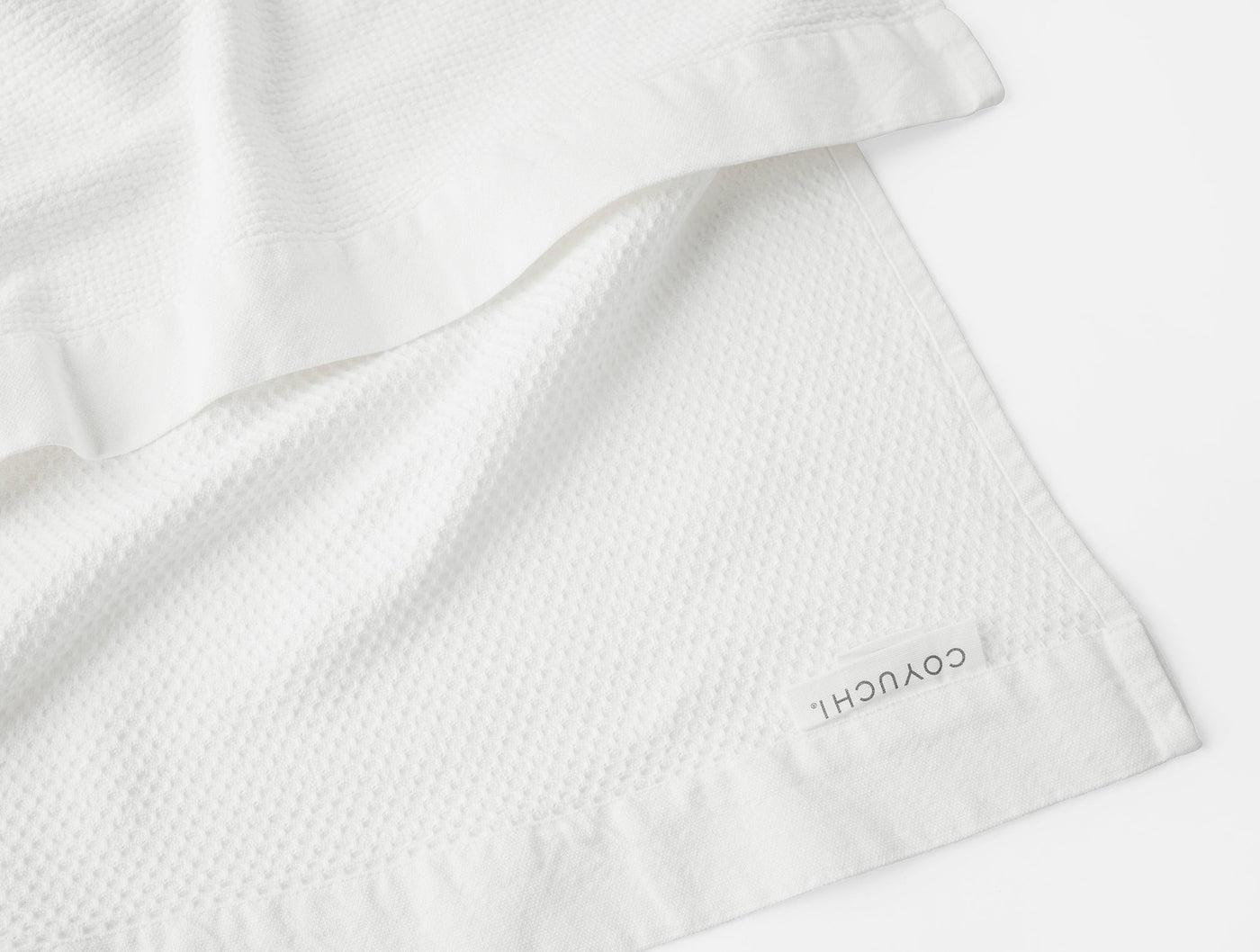 Close-up of Coyuchi Adriatic wash cloth corner showing white waffle texture and satin hem.